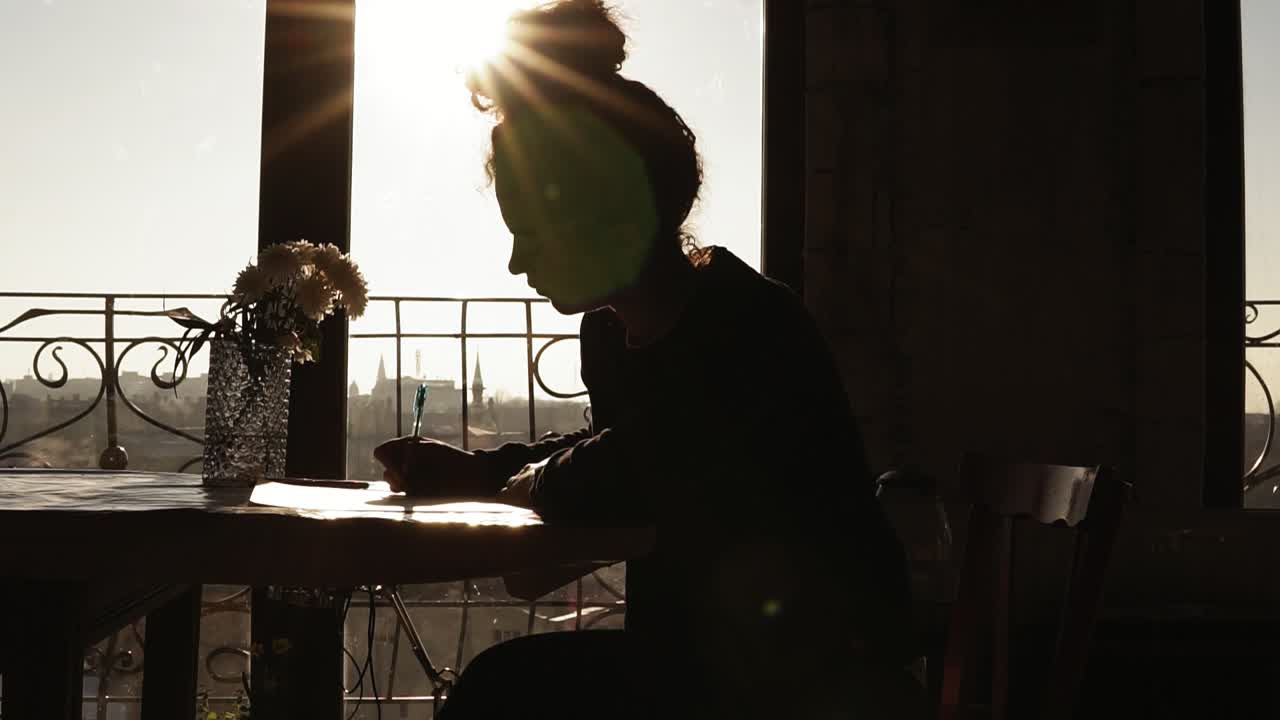 Shaded by the sun, figure of young creativefemale artist drawing something, sitting by the table with beautiful flowers on it. Inspiring art craft.