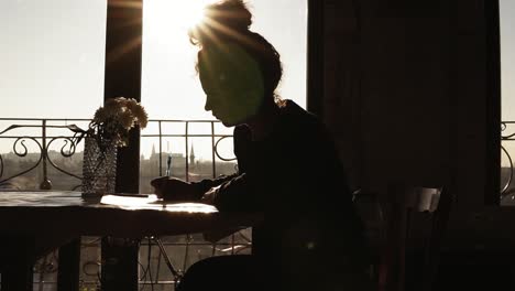 shaded by the sun, figure of young creativefemale artist drawing something, sitting by the table with beautiful flowers on it. inspiring art craft.