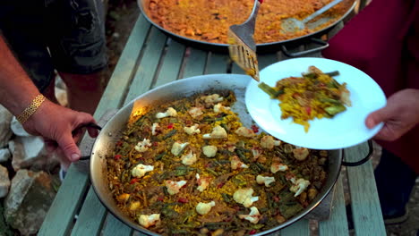 slow motion shot of person putting paella, a common spanish dish, on a white plate, preparing a meal