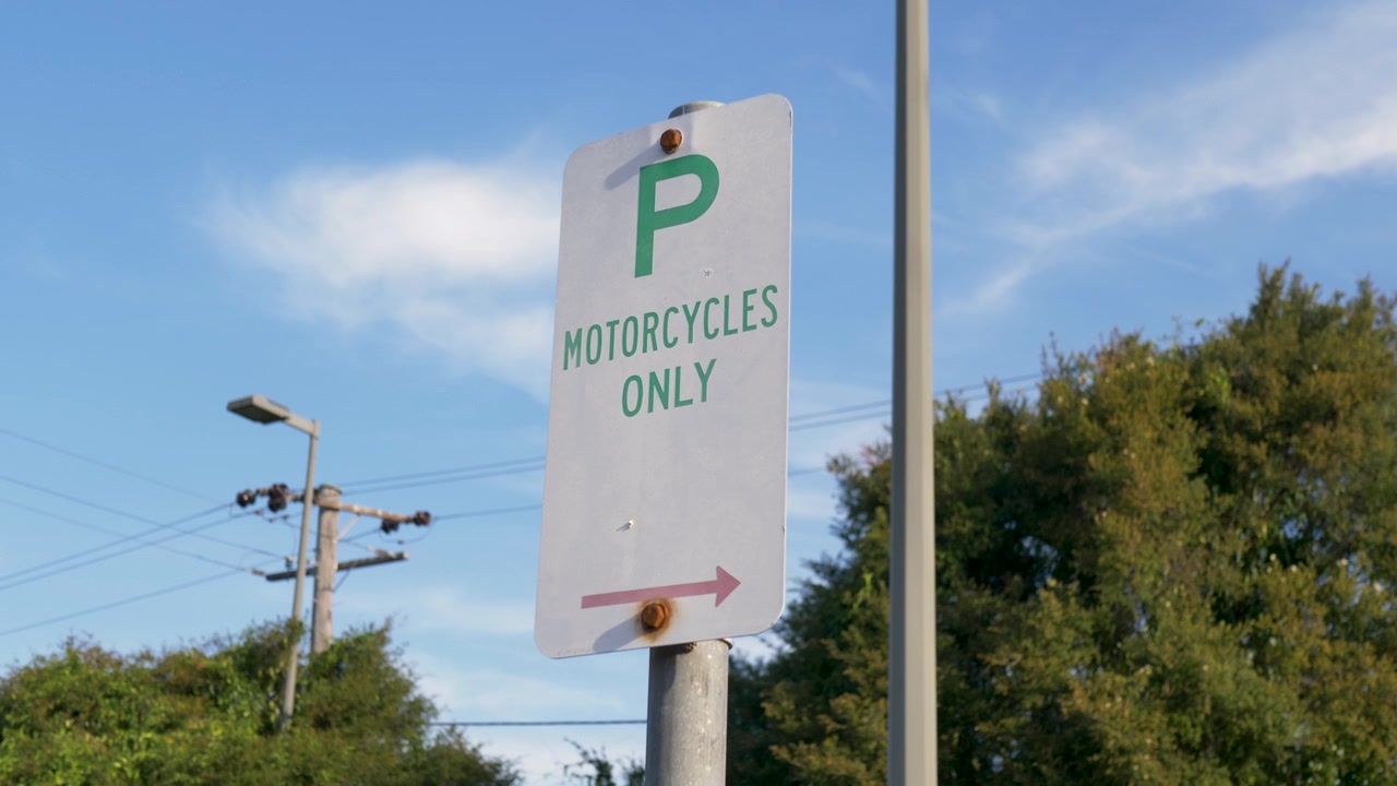 Close-up em câmera lenta de uma placa de estacionamento reservado apenas para motocicletas com uma seta direcional montada em um poste de metal dentro de um estacionamento público no subúrbio de uma cidade rural na Austrália, regras de trânsito