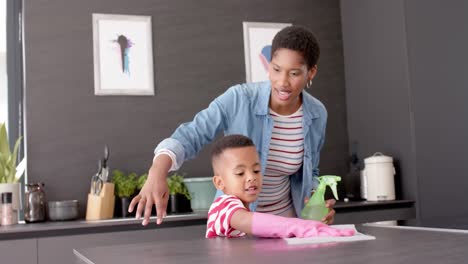 African-american-mother-and-son-cleaning-countertop-in-kitchen,-slow-motion