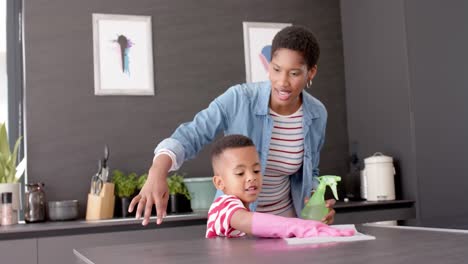 african american mother and son cleaning countertop in kitchen, slow motion