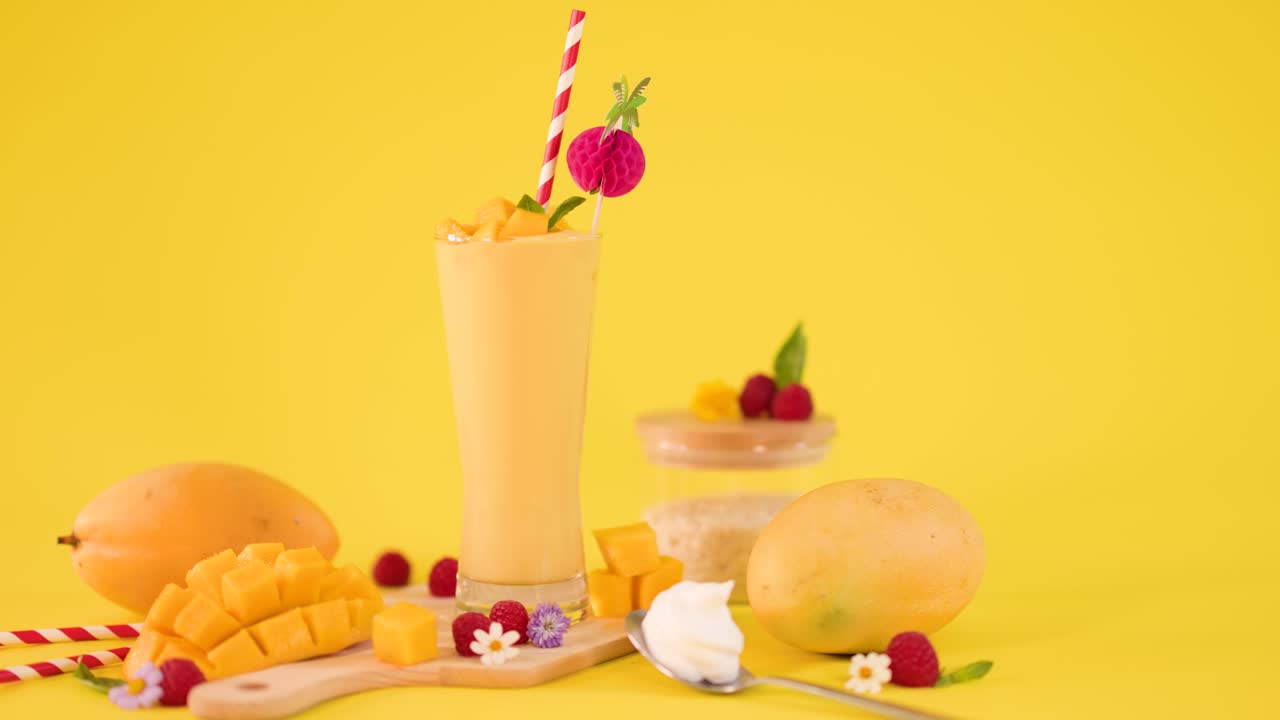 Static close-up of mango smoothie and fresh tropical fruit on bright yellow studio background