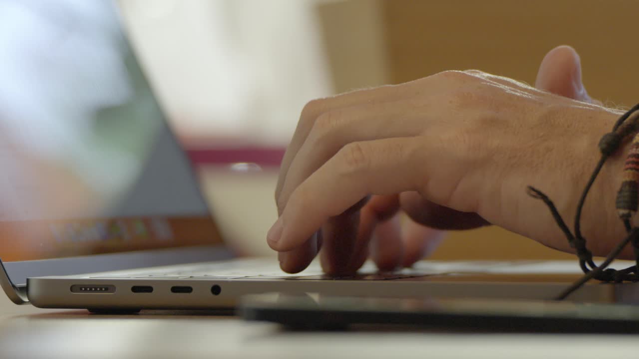 Filmed up close, the hands are tapping on the laptop keyboard