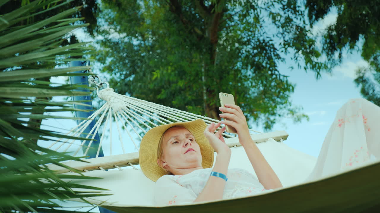 mujer joven descansando en una hamaca usando una conexión de teléfono móvil en concepto de vacaciones video 4k