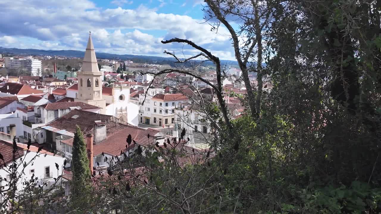 Panoramica a mano sui tetti di tegole rosse e un campanile a Tomar, Portogallo, sotto nuvole gonfie con colline distanti — ideale per temi di viaggio, patrimonio e architettura.
