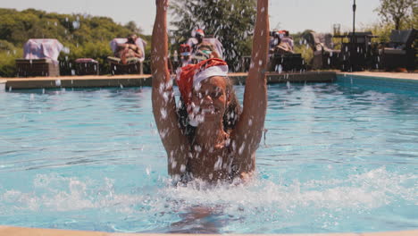 retrato de una mujer en las vacaciones de navidad salpicando en la piscina con sombrero de santa