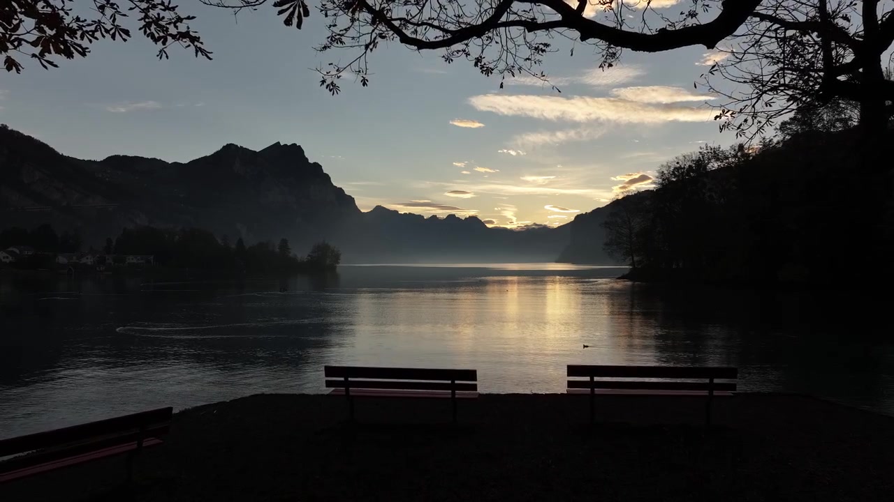 Quiet sunset over Walensee, Switzerland, with benches silhouetted by the lake under trees