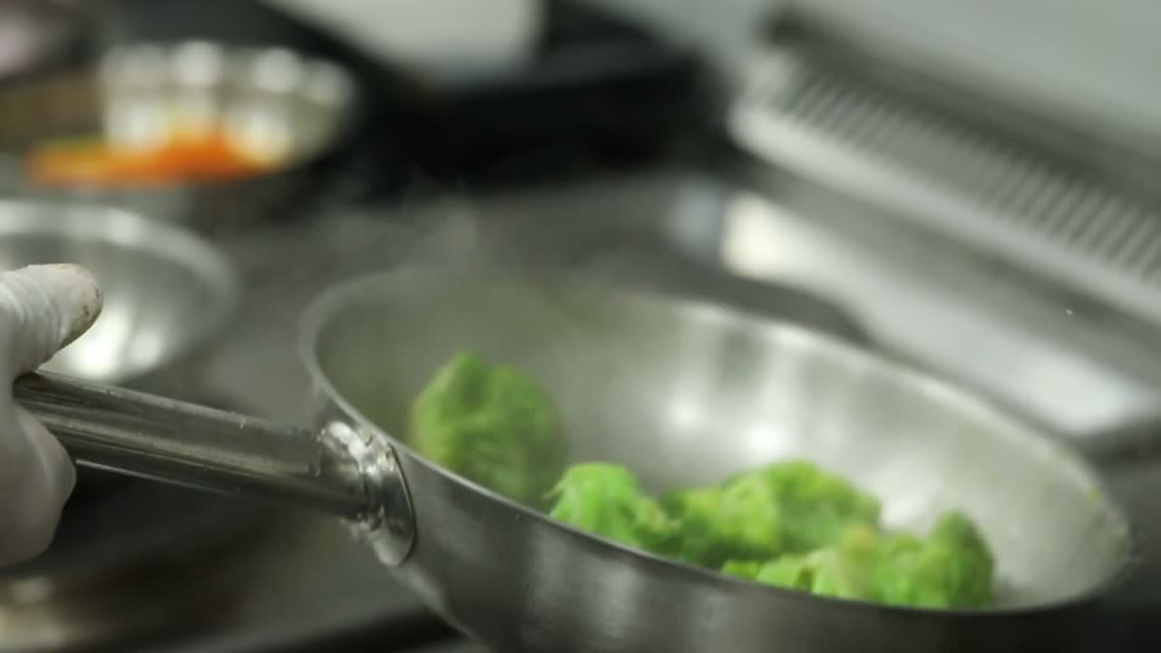 Un cuoco cucina broccoli su una griglia, primo piano, inquadratura di inserimento