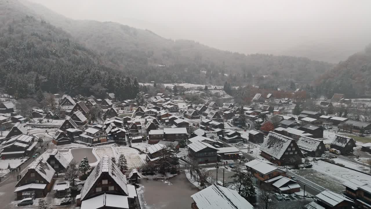 una cautivadora toma de drone de la aldea de shirakawa-go en japón mientras la nieve cae suavemente, cubriendo las icónicas casas gassho-zukuri y el paisaje circundante.