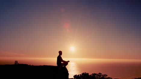 hombre meditando en un acantilado con vistas al océano al atardecer