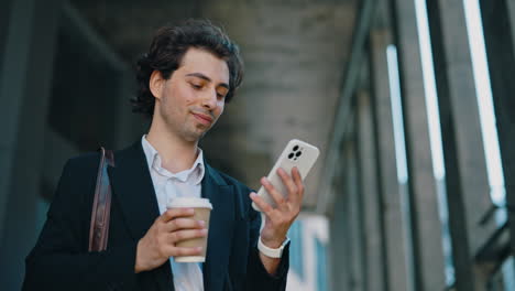 young man using smartphone and holding a coffee cup in an urban setting