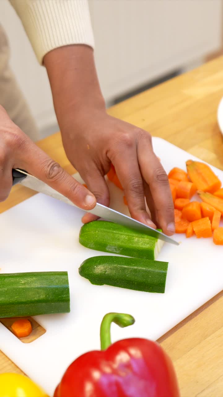 Primo piano di mani che tagliano zucchine fresche su un tagliere bianco
