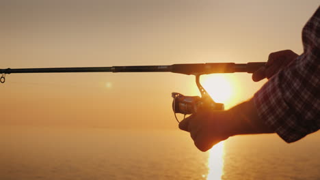 un hombre está pescando en la orilla del mar en el marco los brazos están torcidos por un mango de carrete en el giro