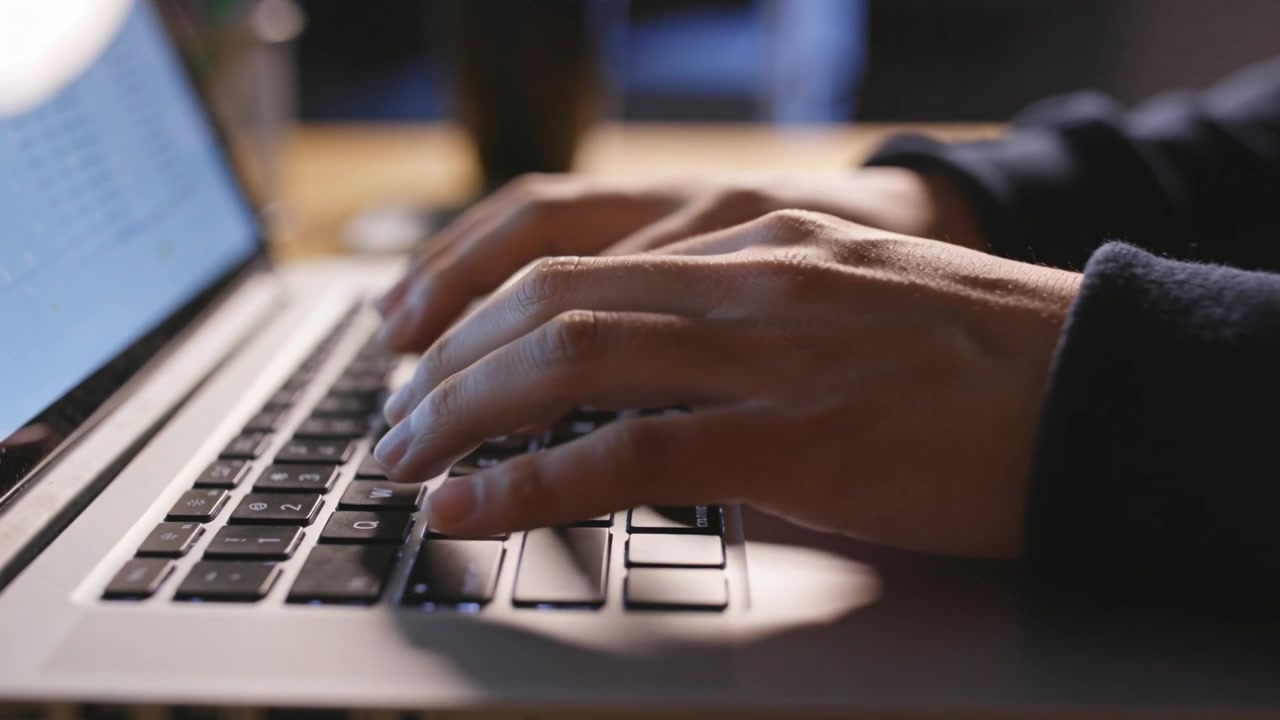 Typing adult hands tapping keys with wrist shifts at desk, prompted by laptop screen, dark sleeves
