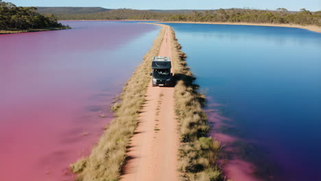 camper van on a causeway between striking pink and blue lakes