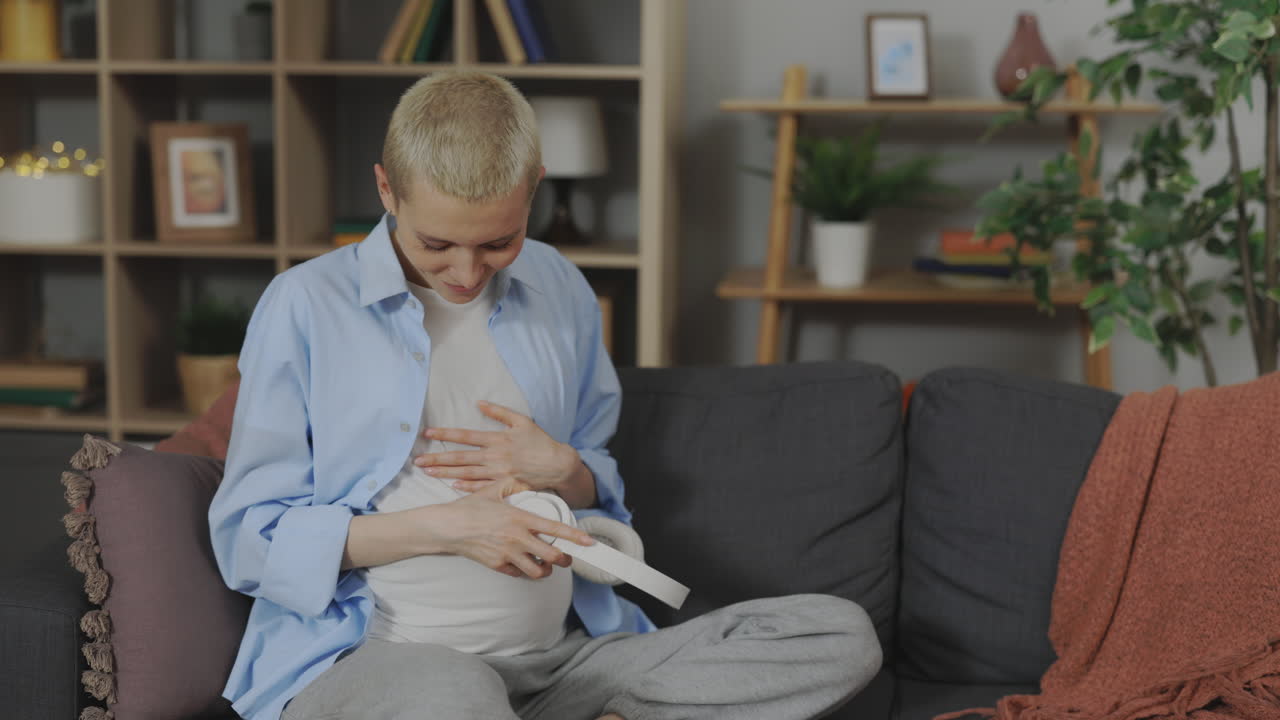 Pregnant woman relaxing with headphones on the sofa