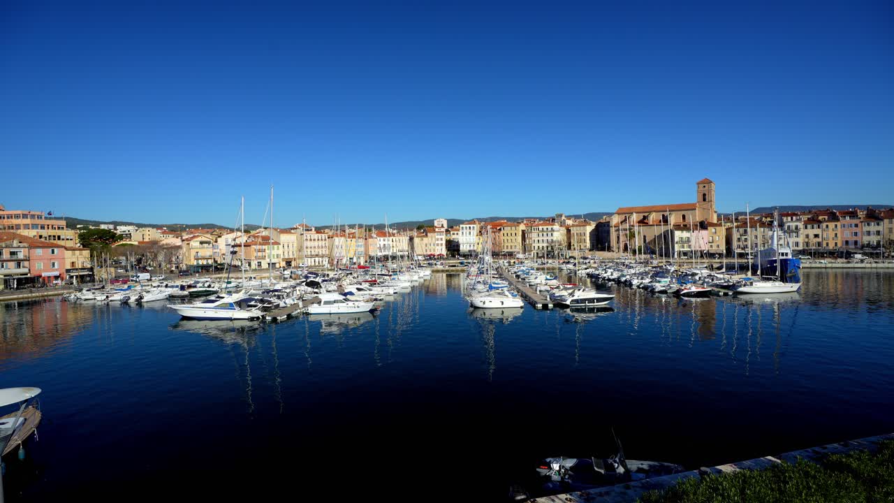 Pemandangan Panorama marina La Ciotat yang dipenuhi perahu layar putih dan yacht yang terpantul sempurna di air tenang dengan latar belakang cakrawala kota bersejarah di bawah langit biru cerah