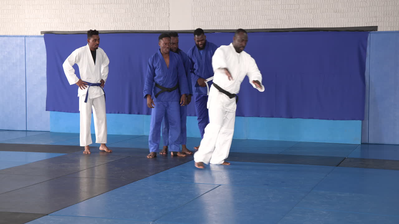 Practicing judo, athlete performing roll on blue mat in dojo