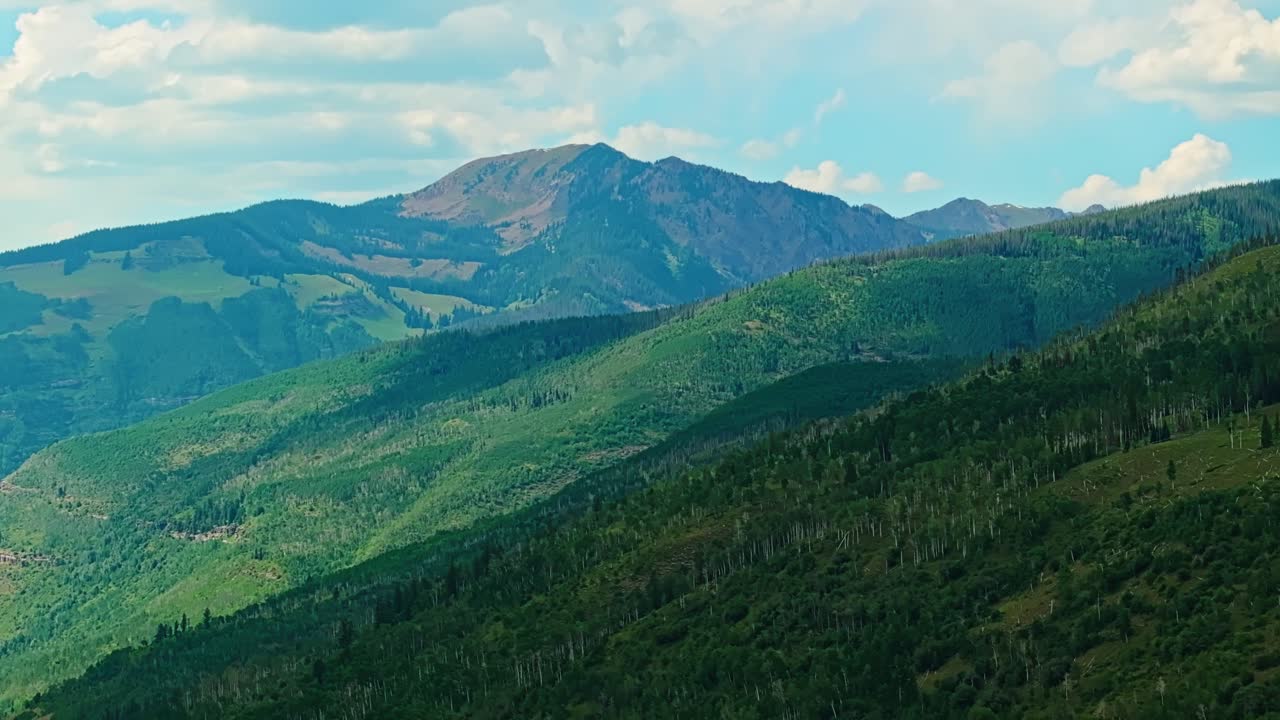 Drone establishing of cloud shadows across Vail terrain with green slopes, tree cover, and distant alpine ridges in summer