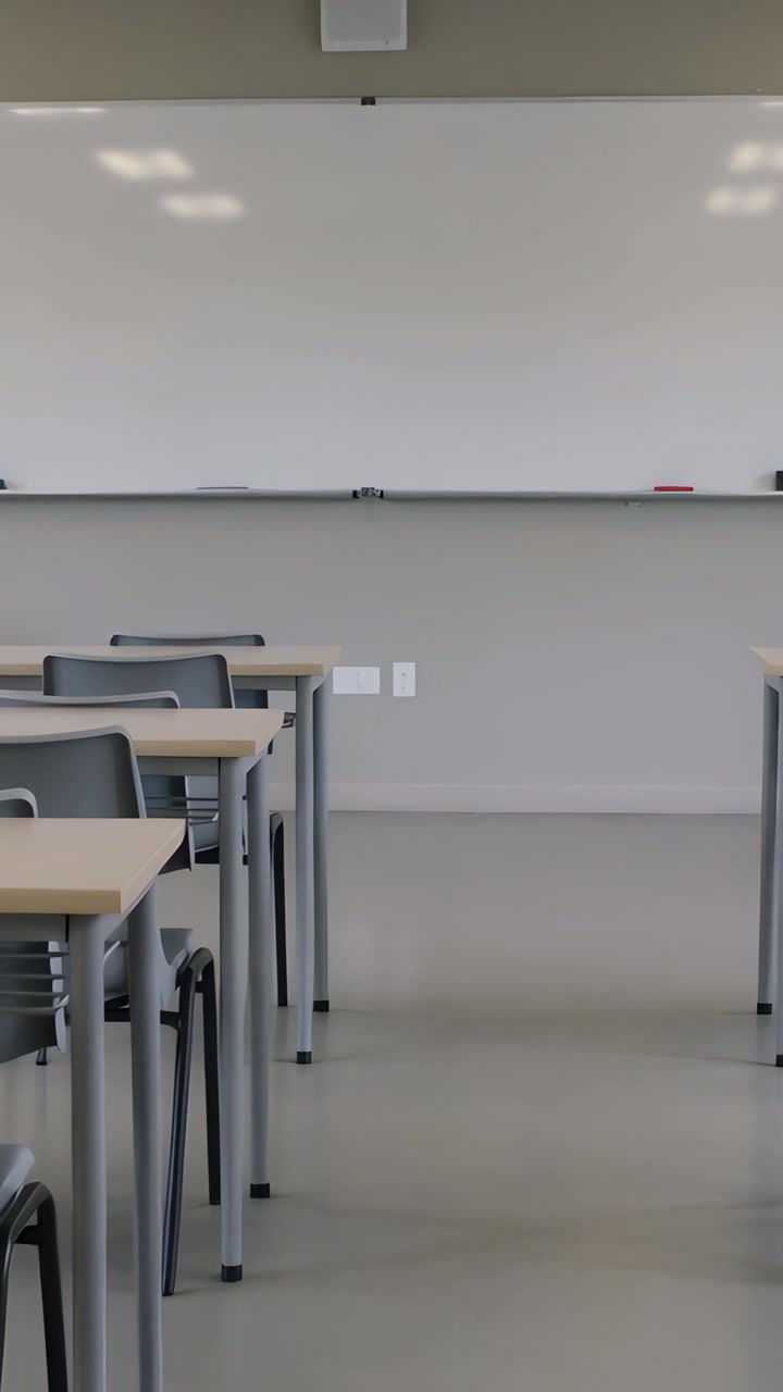 Video verticale: Panoramica in avanti della telecamera a scuola, che mostra una lavagna bianca, un vassoio per pennarelli e banchi allineati.