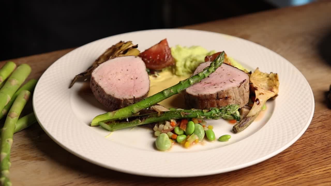 Koki menata tenderloin babi gourmet dengan asparagus dan sayuran.