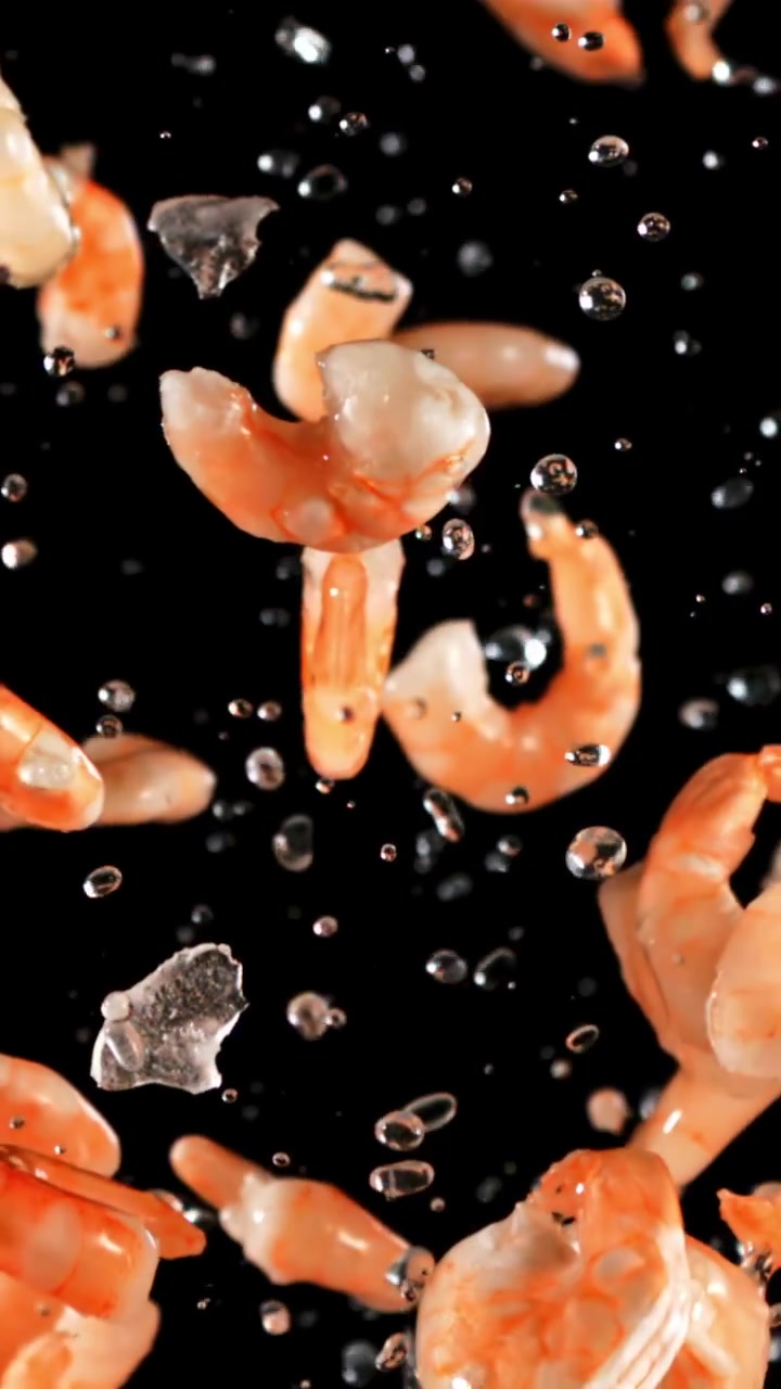 Gamberetti cotti e goccioline d'acqua che cadono al rallentatore su sfondo nero