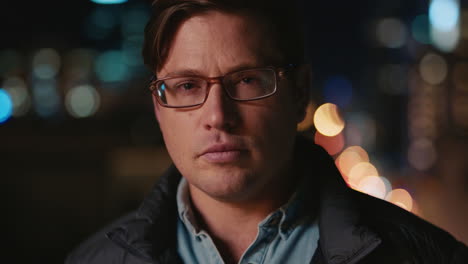 portrait of young caucasian man on rooftop at night wearing glasses with bokeh city lights in urban skyline background