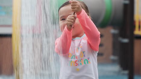 Cara-De-Una-Niña-Feliz-Y-Sonriente-Arrastrando-Alambre-Para-Iniciar-Una-Ducha-De-Agua,-La-Madre-Sostiene-La-Pierna-Desnuda-Bajo-Agua-Vertida-Salpicándola-En-Cámara-Lenta