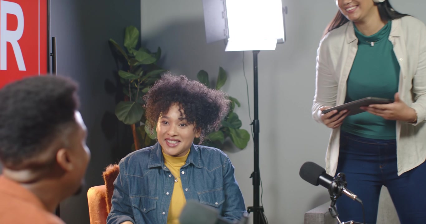 Afroamerikanske værter i studie rækker tablet, siddende vært gennemgår noter, leder interview.