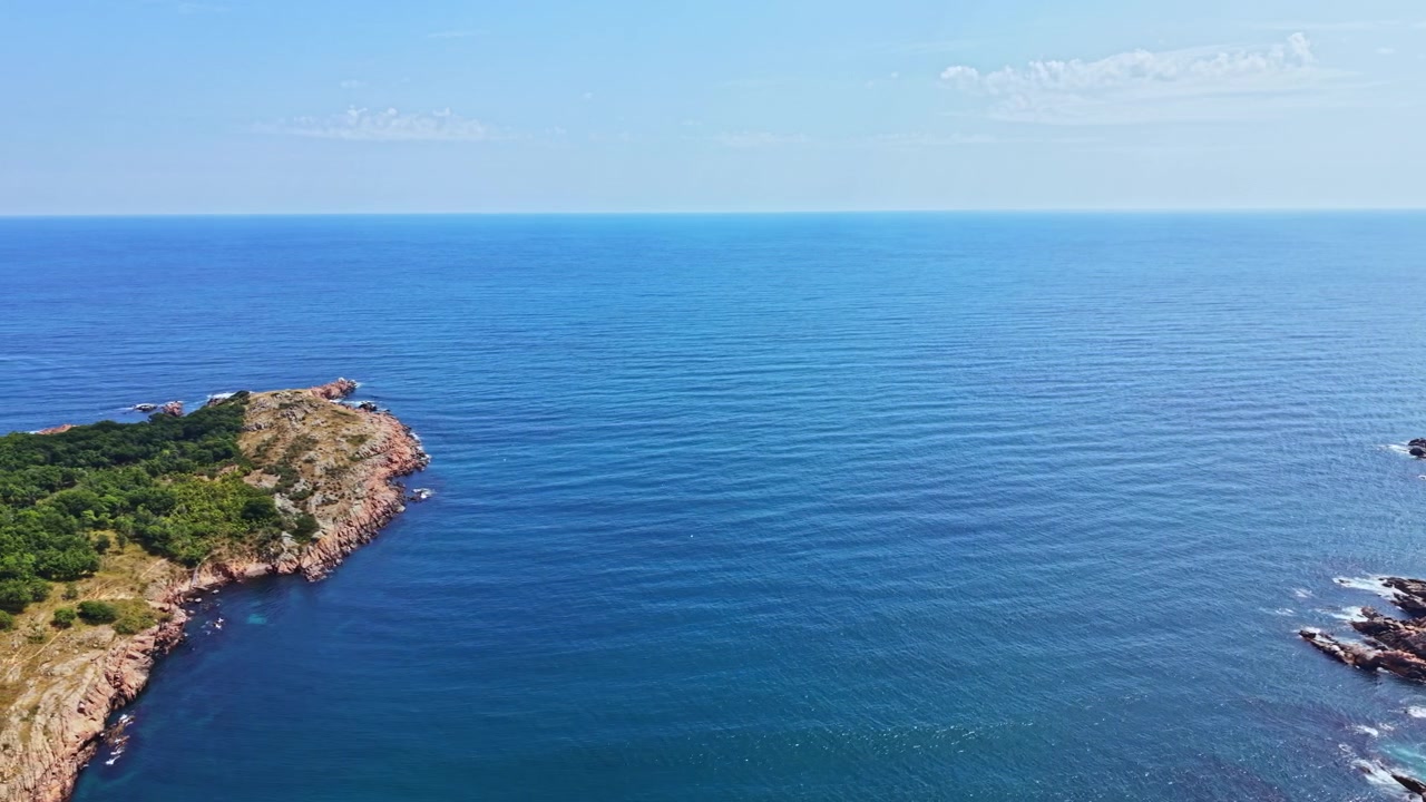 Oceano blu che incontra la costa rocciosa sotto un cielo sereno durante il giorno.