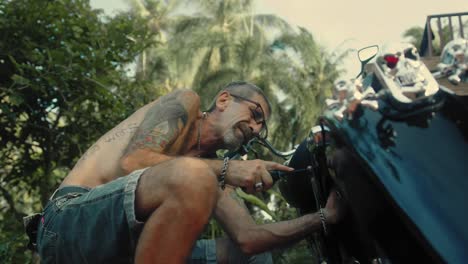 man repairing a classic motorcycle in a tropical garden
