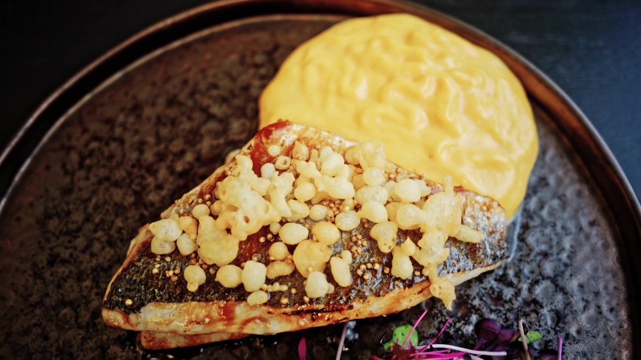Nærbilde av en pannestekt hvit fiskefilet med sprøtt skinn, toppet med sprø puffede korn