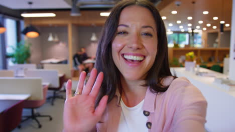 pov selfie portrait of businesswoman in modern office waving to mobile phone camera