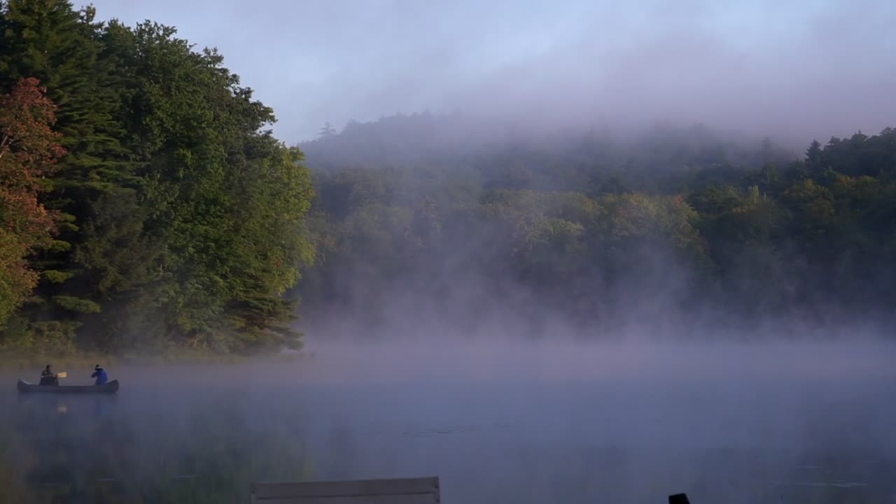 a fishing canoe over a misty pond on a foggy morning
