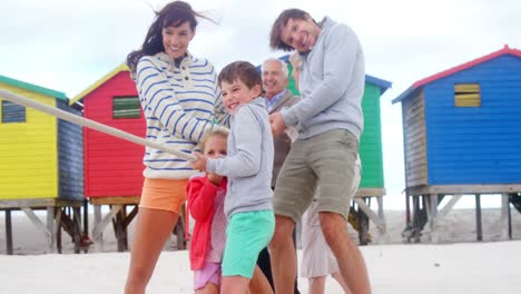 multi generation family playing tug of war at beach