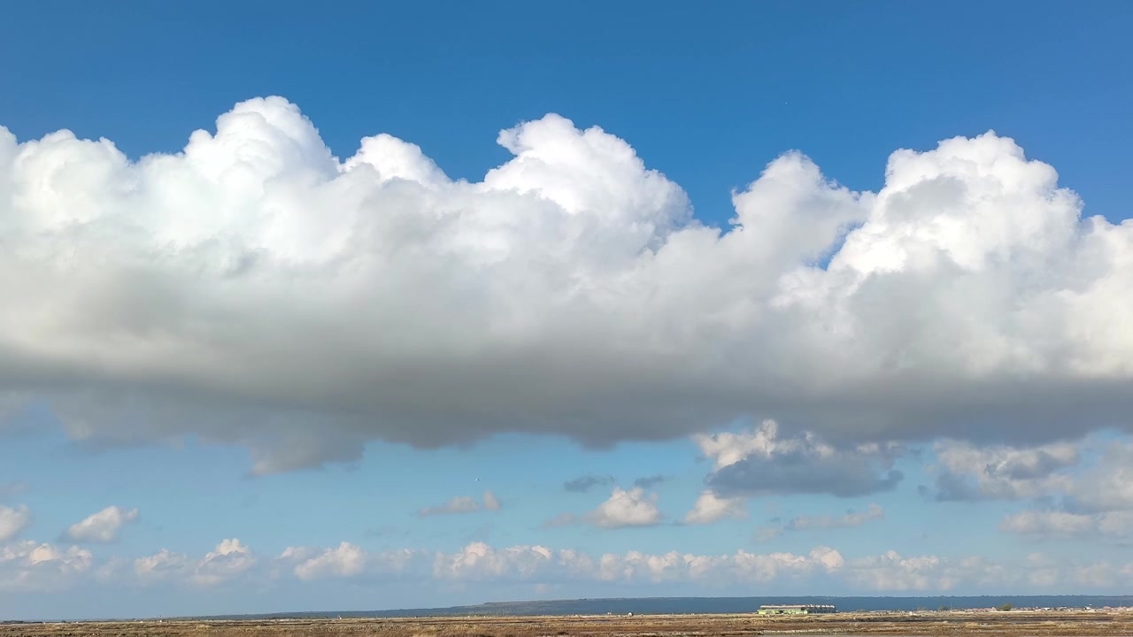 Large White Cumulus Clouds Drifting Over a Flat Coastal Landscape