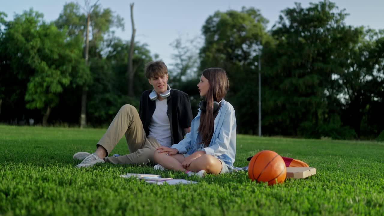 una pareja joven sentada en la hierba y hablando.