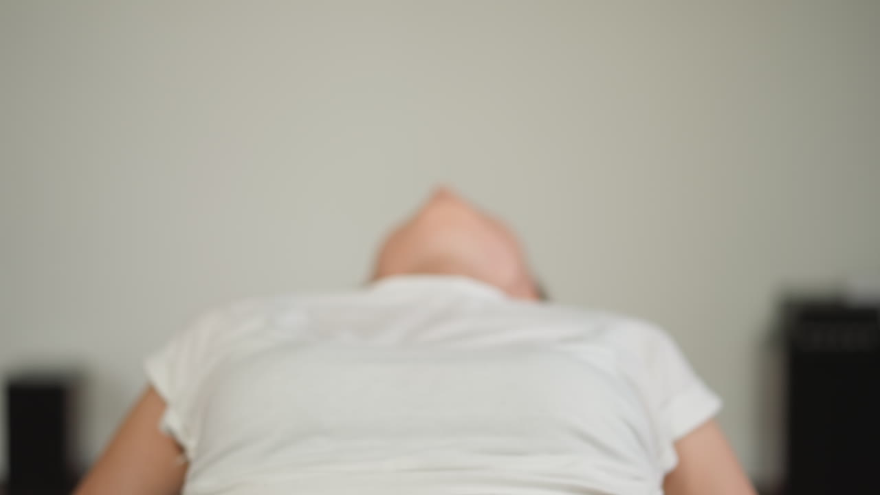 여성은 집에서 공으로 허리 근육을 운동합니다. 여성은 구부러진 위치에서 몸을 들어 올립니다. 운동복을 입은 평온한 여성은 개인 공간에서 운동 공에서 운동을 즐니다.