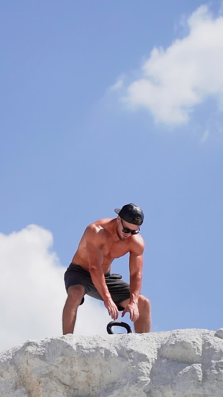 Healthy athlete taking up heavy kettlebell outdoors. Fitness training man lifting weight on the top of white mountain. Slow motion. Vertical video