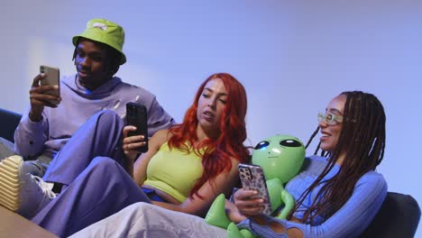 fotografía de estudio de un grupo de amigos de la generación z sentados en el sofá jugando y usando las redes sociales en los teléfonos móviles 3