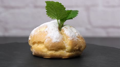 baked custard eclairs and sprinkled with powdered sugar and decorated with a mint leaf on a black board