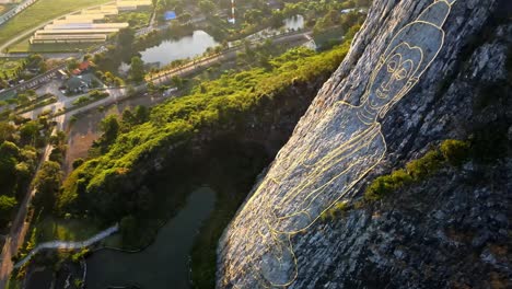 4k drone pans izquierda se inclina hacia arriba en la imagen tallada de buda hecha de oro en un acantilado en khao chee chan, pattaya, tailandia
