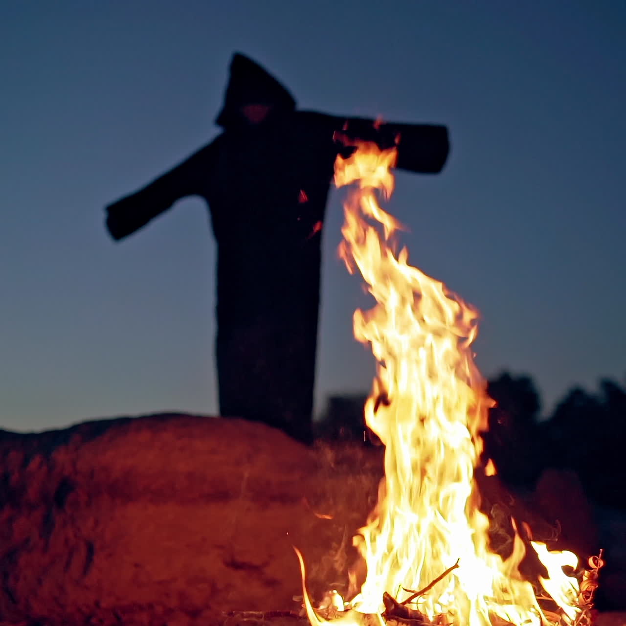 Evil witch in black cloak with hood near the fire. Halloween costume.