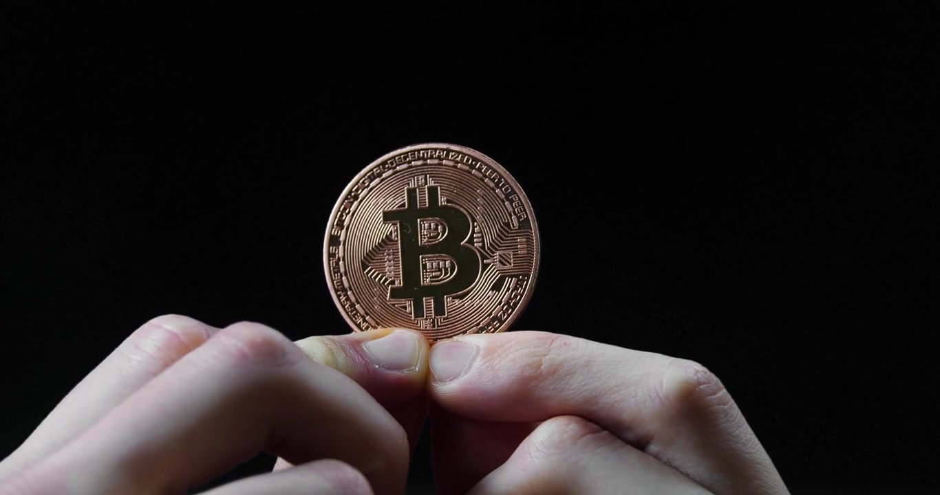Due mani che tengono e mostrano una moneta di criptovaluta Bitcoin su sfondo nero per temi finanziari