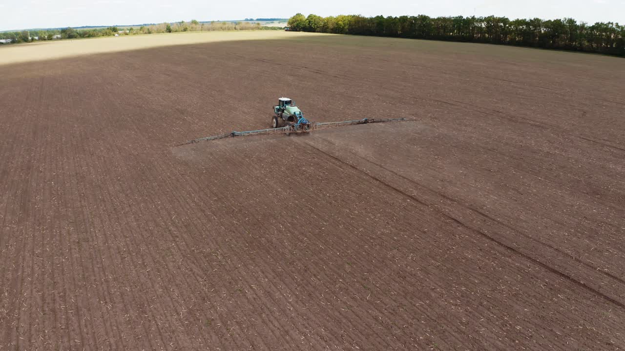Agricultural field in spring. Tractor with special equipment spraying field. Flying over the field with machinery sprinkling chemicals during seasonal works. Aerial view.