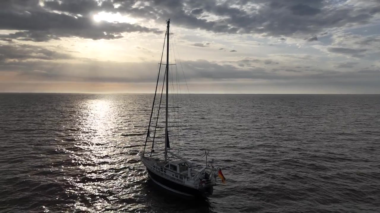 Dron realiza una órbita circular lenta alrededor de un velero mostrando una vista lateral en mar abierto