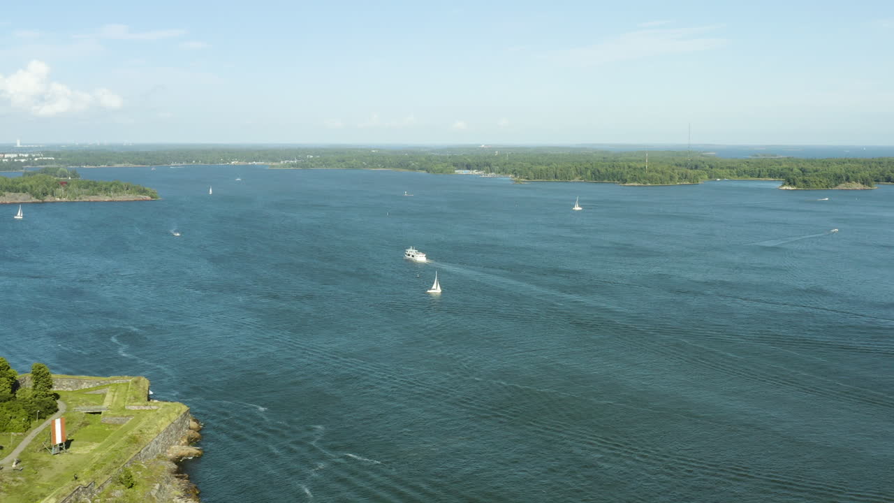 vista aérea de un ferry y veleros, en la costa de la isla de suomenlinna, soleado día de verano, en helsinki, finlandia - seguimiento, disparo con drones