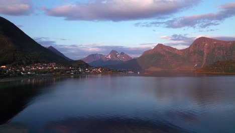 aerial panning shot of a small town nestled in a fjord along the cost of norway during a beautiful sunset with mountains and clouds