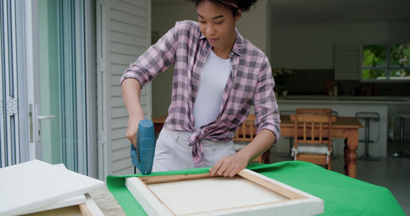 Posizionando una cornice su tessuto verde, donna afroamericana che tira e pinza con una pinzatrice blu